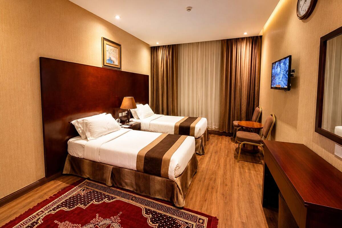 Habitación de hotel con dos camas, un escritorio, una silla, un televisor y un reloj en la pared.
