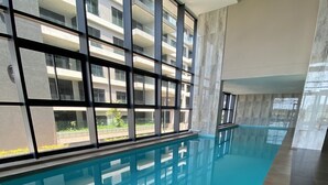 Uima-allas, jossa on laatoitettu pohja, suuret ikkunat ja näkymä korkeaan kerrostaloon.