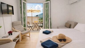 Ein Hotelzimmer mit Bett, Sessel, kleinem Tisch und einem Balkon mit Tisch und Sonnenschirm.