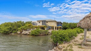 A two-story house with a balcony, located near a body of water with vegetation. - The Peninsular House – Private Waterfront Paradise (Marathon)