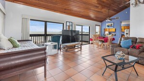 A spacious living area with a large TV, wooden ceiling, and a balcony with a view. - The Peninsular House – Private Waterfront Paradise (Marathon)