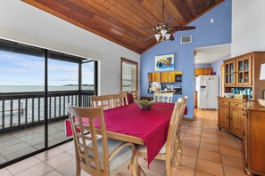 A dining area with a table and chairs, a view of the sea, a kitchen with cabinets, and a ceiling fan. - The Peninsular House – Private Waterfront Paradise (Marathon)