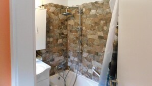 Un baño con pared de piedra, ducha, lavamanos e inodoro.