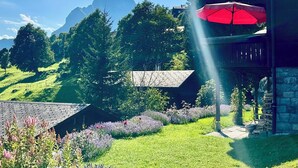 Uma casa com um guarda-sol vermelho, uma parede de pedra e um jardim com diversas plantas.
