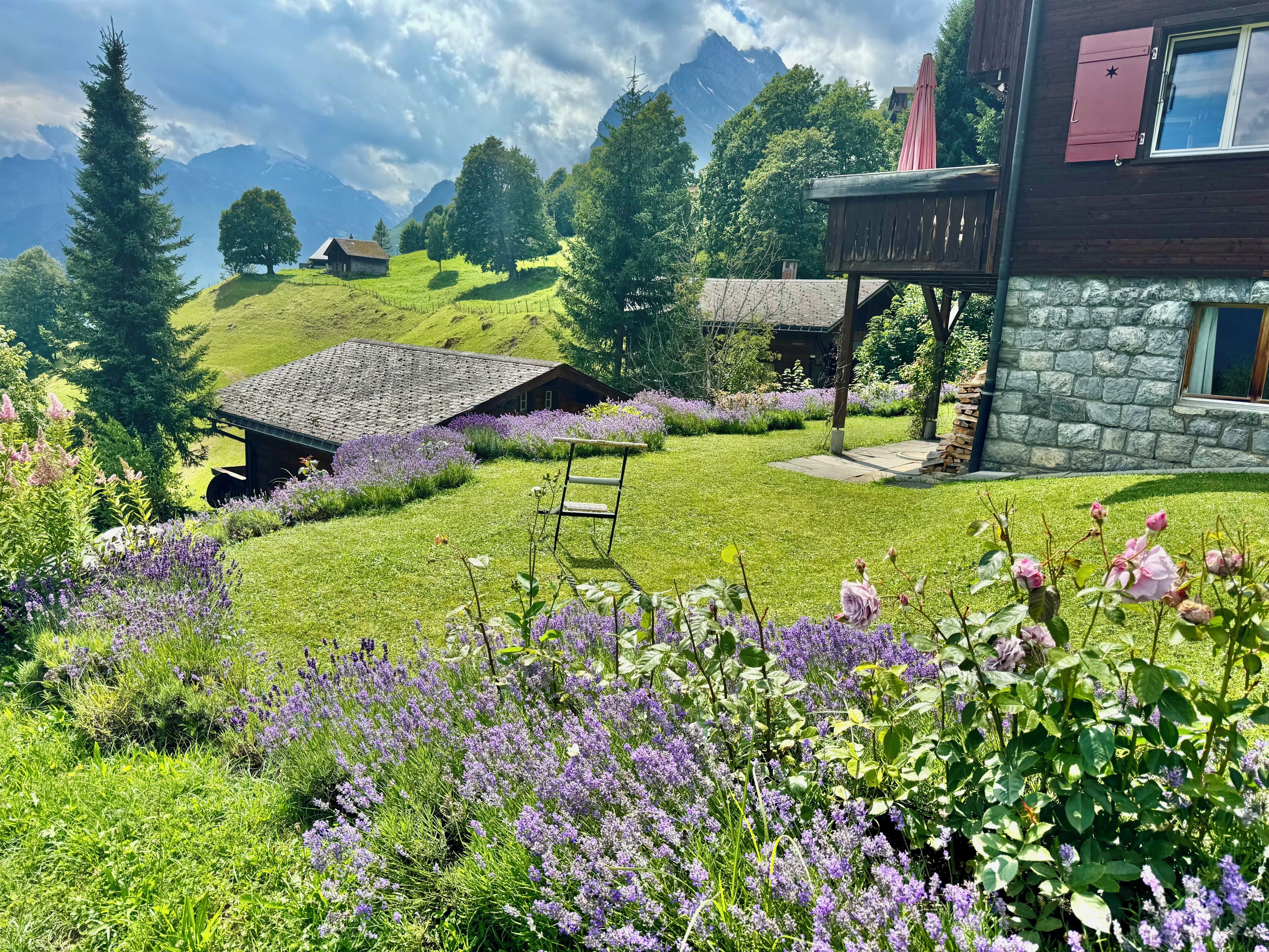 A rustic house with a stone wall, a wooden deck, and a view of mountains.