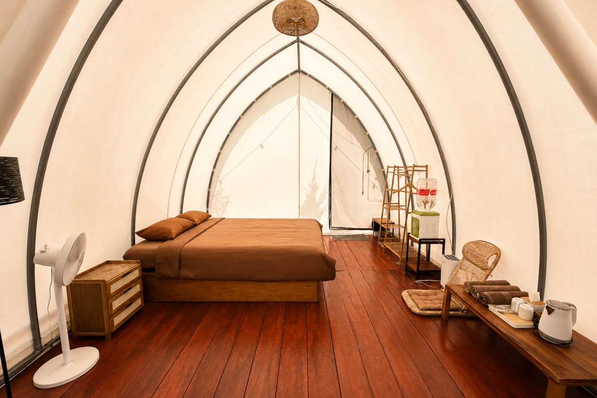 Habitación tipo alojamiento en tienda de campaña con cama, suelo de madera, un ventilador, una mesa con toallas y una escalera.