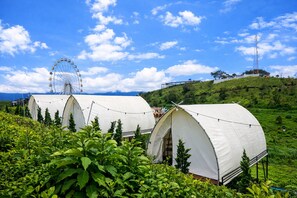 Une rangée de tentes blanches, avec une grande roue et une colline en arrière-plan.