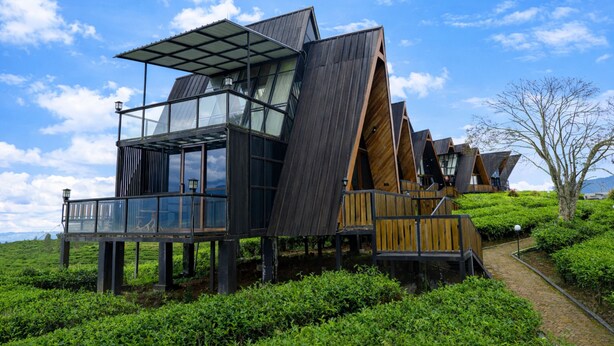 Una estructura moderna de madera, de varios niveles, con ventanales de vidrio y techo metálico, ubicada en una verde ladera.