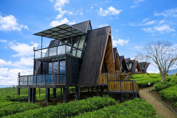 Eine moderne, mehrstöckige Holzkonstruktion mit Glasfenstern und einem Metallroof, gelegen an einem üppigen, grünen Hang.