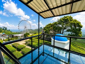 A glass-enclosed balcony with a view of a Ferris wheel, a blue dome structure, and lush greenery. - Nimo Tea Resort (Pangalengan)