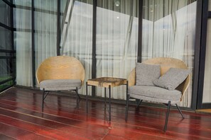 Deux fauteuils gris, recouverts de tissu, avec des accoudoirs en bois, et une petite table en bois placée entre eux, le tout posé sur un plancher en bois rouge, avec une grande fenêtre en arrière-plan.