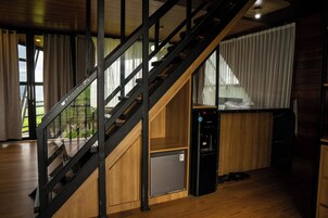 A staircase with a glass railing, a compact refrigerator, and a wooden cabinet in a room with large windows and a wooden floor.
