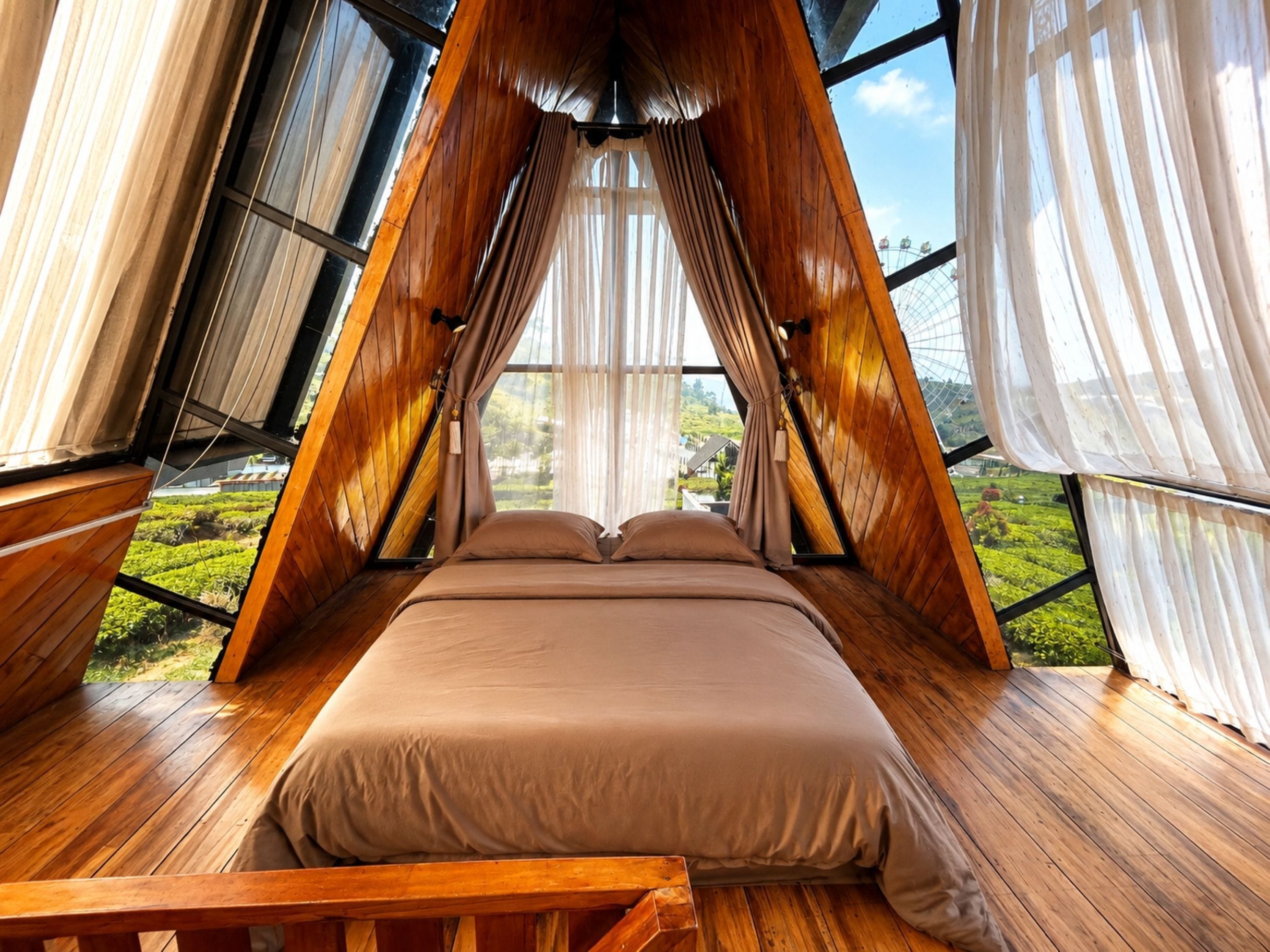 A room with a bed, wooden flooring, and large windows.