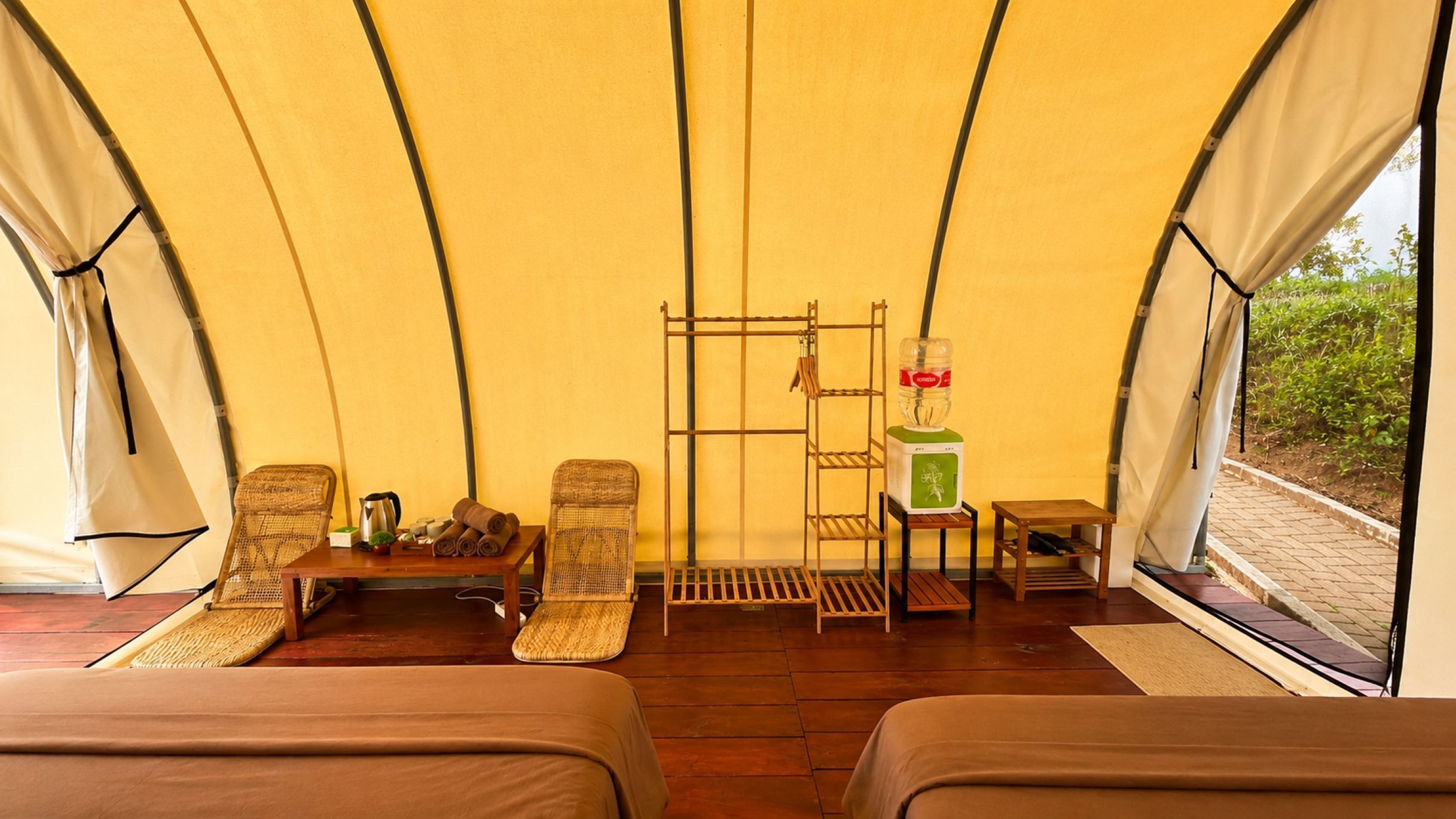A tented accommodation with two beds, a table with a kettle, and a chair.