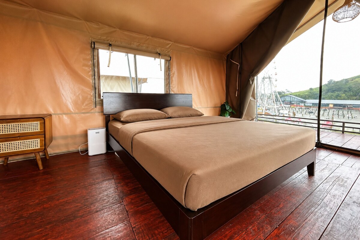 Un dormitorio con una cama grande, una mesita de noche, una lámpara y vistas a un espacio exterior.