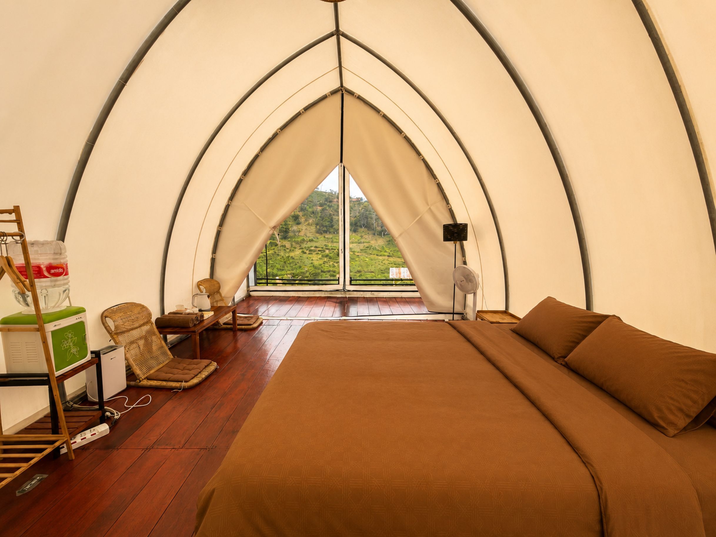 A tented accommodation with a bed, seating area, and a view of the outdoors.