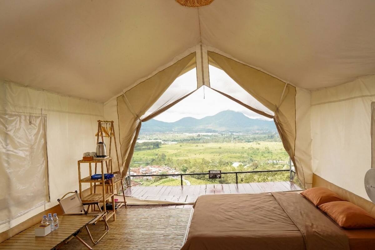 A tented room with a bed, a small table, and a view of a green landscape.