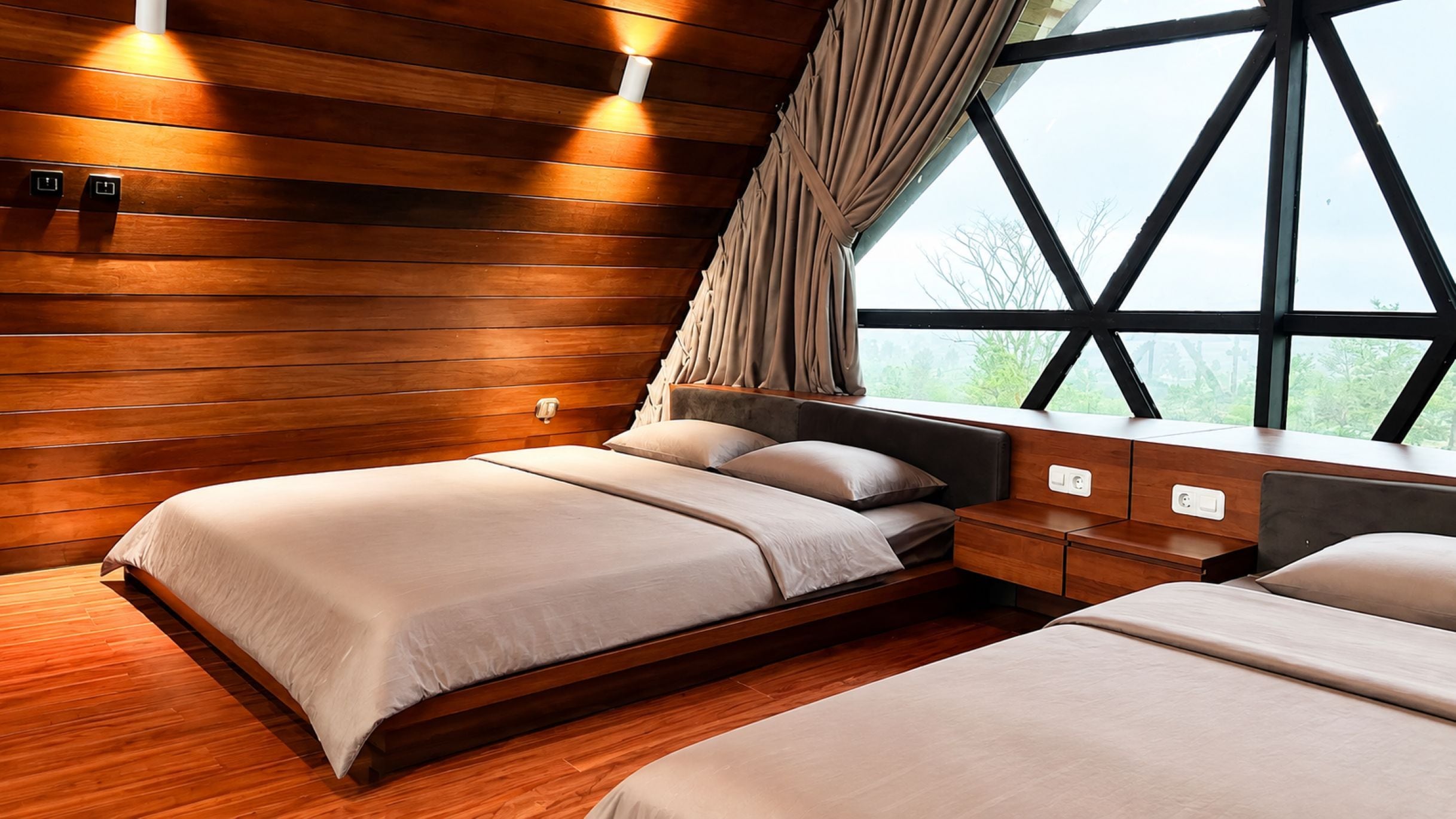 Ein Schlafzimmer mit zwei Betten, Holzwänden, einem Fenster mit Vorhängen und einem Nachttisch mit Lampe.