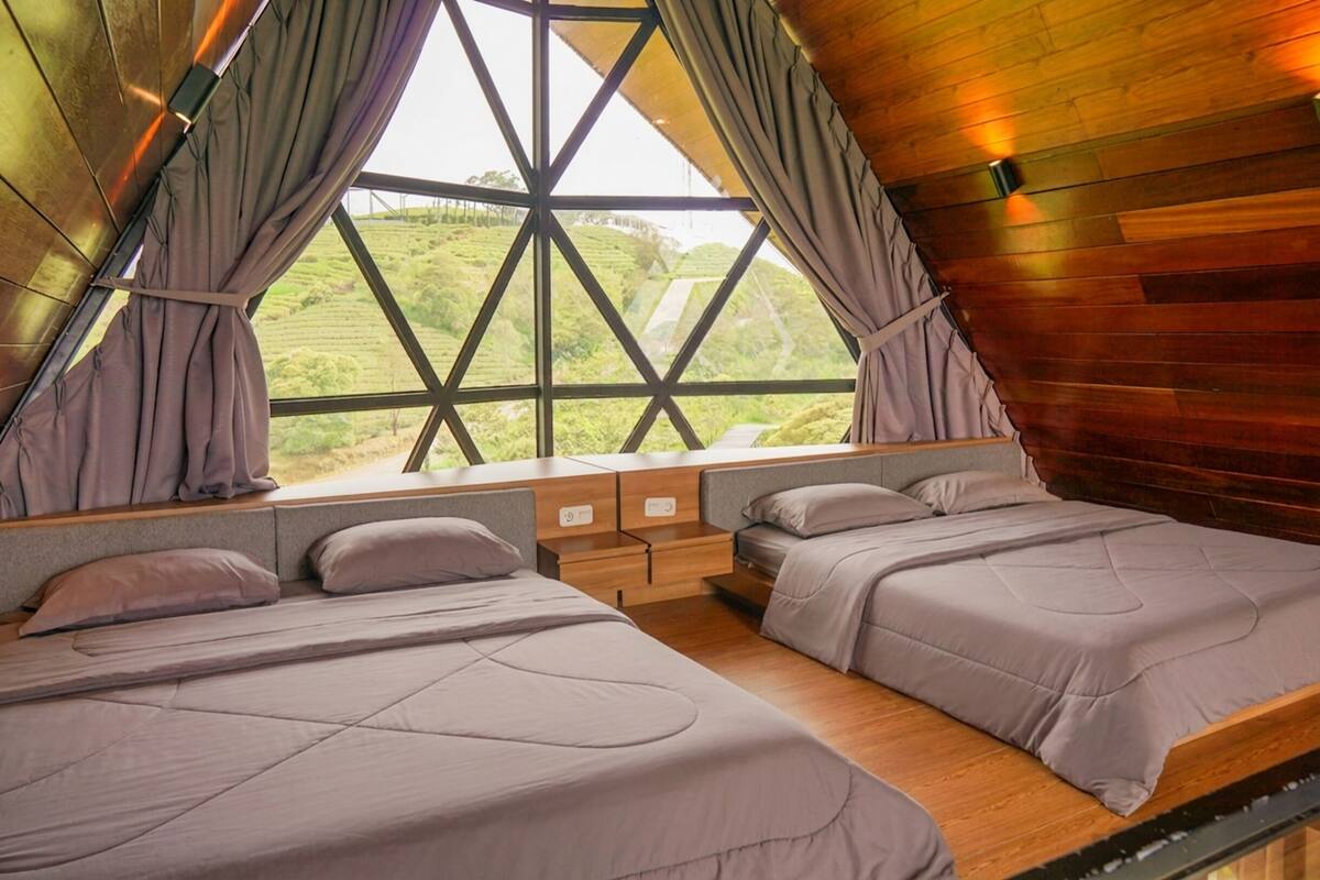 A room with two beds, a window with curtains, and a view of green hills.