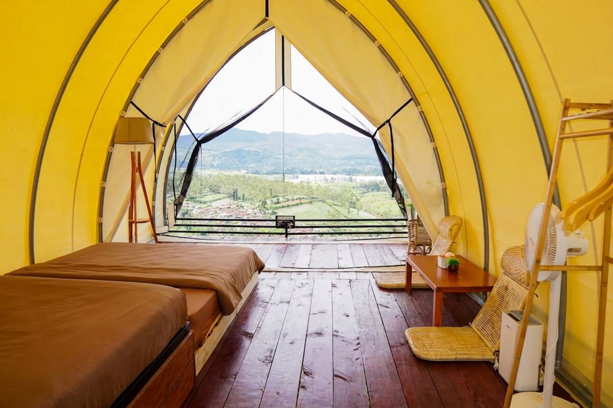 A tent with a bed, a table, and a chair, with a view of a landscape.