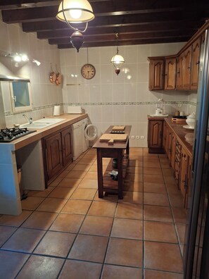 Een keuken met een fornuis, spoelbak, houten kastjes, een klok en een tafel met een blender.