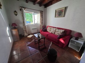 Una sala de estar con un sofá rojo, una mesita, un banco, una lámpara y un cuadro en la pared.