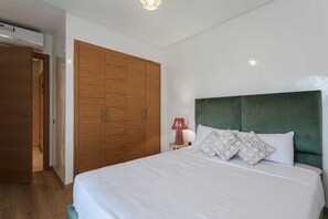 Ein Schlafzimmer mit einem Bett, einem mit grünem Stoff gepolsterten Kopfteil, einem Holzschrank und einer Nachttischlampe.