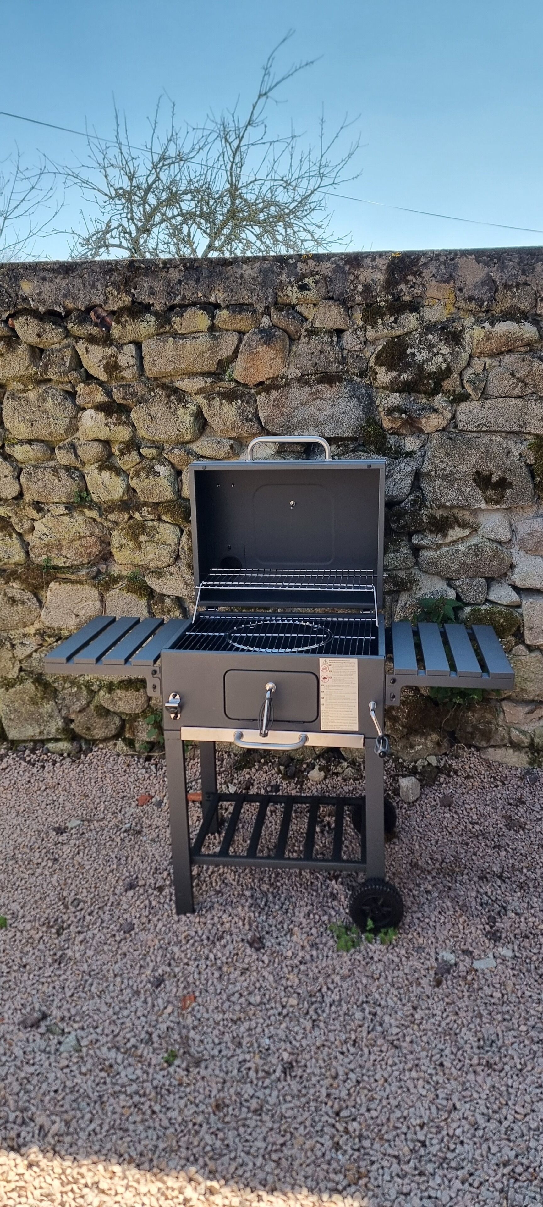 A portable grill with a metal grate, a handle, and a control panel, set against a stone wall background.