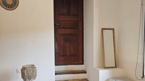 A staircase with a wooden door, a white bedside table with a lamp, a small white appliance, and a hexagonal tiled floor. - Small apartment in the village (Lauris)