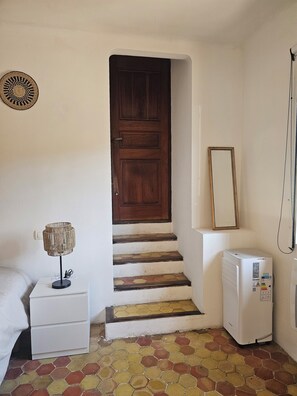 Eine Treppe mit einer Holztür, ein weißer Nachttisch mit einer Lampe, ein kleines weißes Gerät und ein sechseckig gefliester Boden.