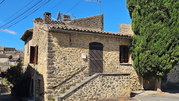 A stone building with a tiled roof, a wooden door, and a small staircase leading to the entrance. - Small apartment in the village (Lauris)