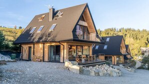 A modern house with a sloped roof, large windows, and a wooden deck. - Large Holiday Villa With Sauna and Mountain Views (Bukowina Tatrzanska)