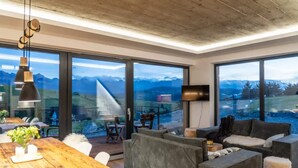 A modern living room with a wooden table, grey sofas, and large windows offering mountain views. - Large Holiday Villa With Sauna and Mountain Views (Bukowina Tatrzanska)