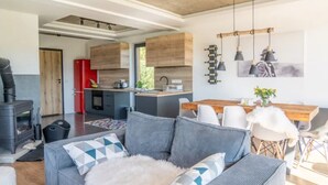 A modern living space with a sofa, a dining table, and a kitchen area with wooden cabinets and pendant lights. - Large Holiday Villa With Sauna and Mountain Views (Bukowina Tatrzanska)