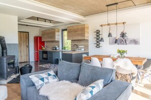 A modern living space with a sofa, a dining table, and a kitchen area with wooden cabinets and pendant lights. - Large Holiday Villa With Sauna and Mountain Views (Bukowina Tatrzanska)