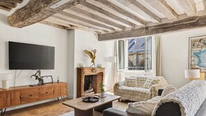 A living room with a fireplace, a sofa, a coffee table, a TV, and a wooden cabinet. - Authentic and Large 1 bdr Flat - Facing Notre Dame (Paris)