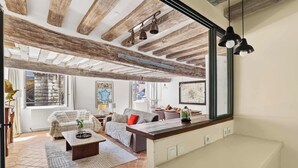 A spacious living room with exposed wooden beams, a large window, and a view of the outdoors. - Authentic and Large 1 bdr Flat - Facing Notre Dame (Paris)