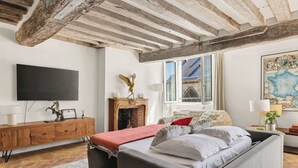 A room with a bed, a wooden cabinet, a fireplace, a map on the wall, and a large window. - Authentic and Large 1 bdr Flat - Facing Notre Dame (Paris)
