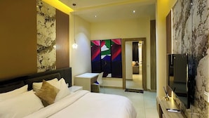 Ein modernes Hotelzimmer mit einem großen Bett, einem Schreibtisch, einem Fernseher und einem durch eine Glastür einsehbaren Badezimmer.