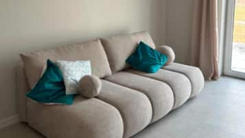 Un sofá color beige con dos almohadones azul turquesa y un cojín redondo decorativo.