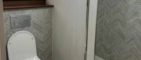 A bathroom with a toilet, a wall-mounted flush handle, and a window with blinds.