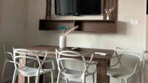 Ein Essbereich mit Holztisch, weißen Stühlen, einem flachbildfernseher, der darüber angebracht ist, und einer Vase mit Dekorationen auf dem Tisch.