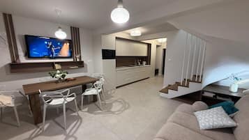 Una sala de estar moderna con sofá, una mesa de comedor y sillas, una zona de cocina con armarios y un microondas, y una escalera que lleva a otro nivel.