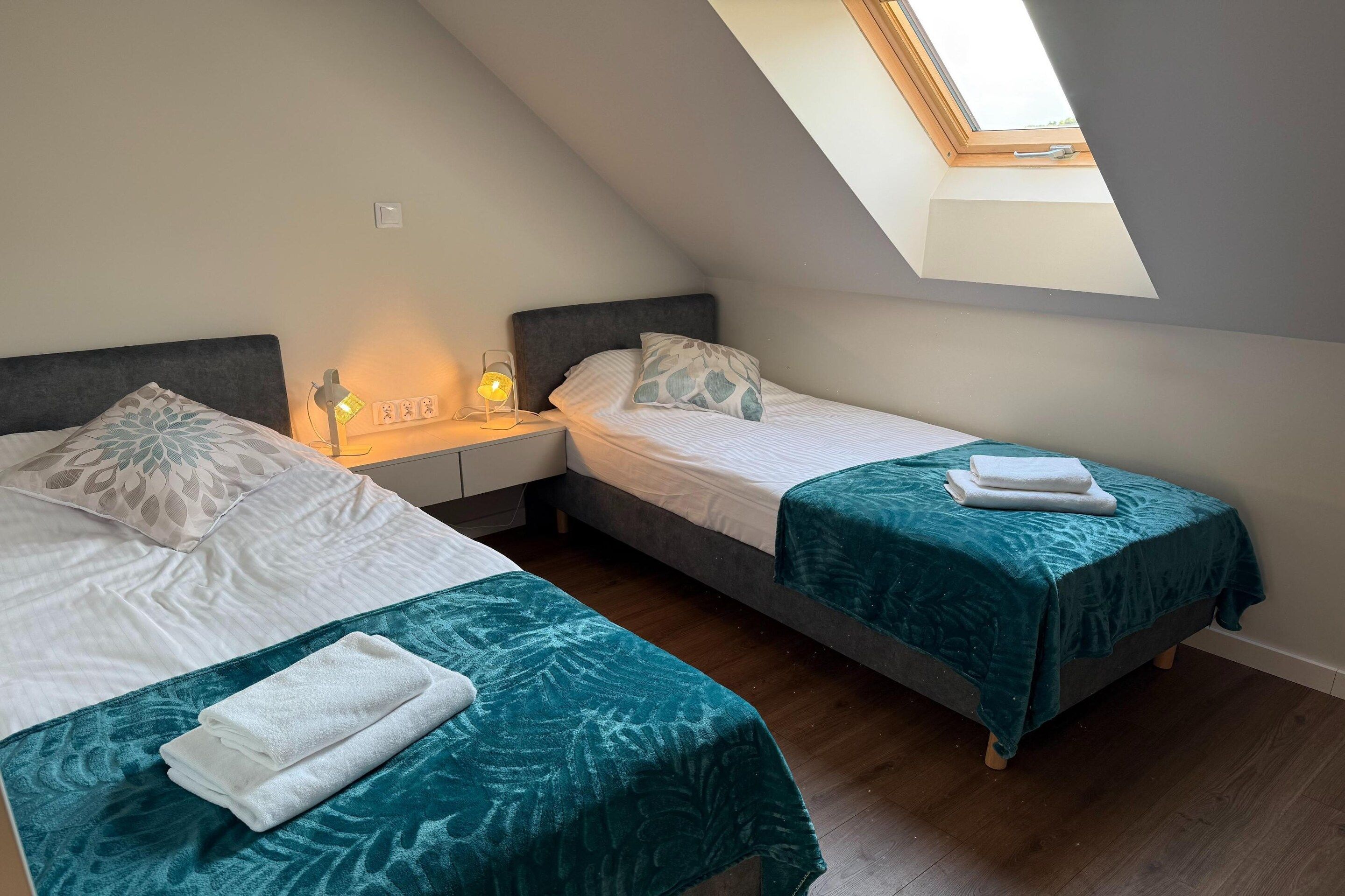 A small, cozy room with two beds, a skylight, and a bedside table with a lamp.