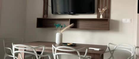 A dining area with a wooden table, white chairs, and a flat-screen TV mounted on the wall.