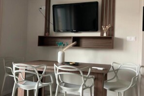 Un comedor con una mesa de madera, sillas blancas y un televisor de pantalla plana montado en la pared.