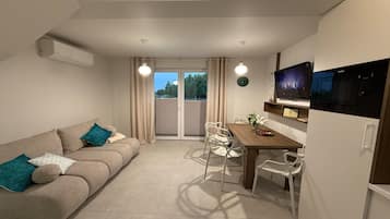 A compact living space with a sofa, dining table, chairs, a TV, and a kitchen area.