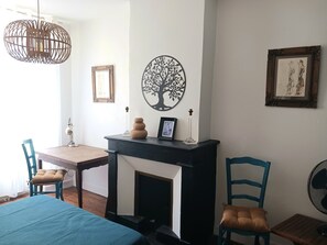 Ein Zimmer mit Kamin, Esstisch, Stühlen, einer Pendelleuchte und Wandbildern.