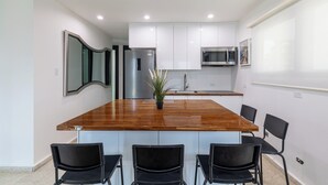 Eine moderne Küche mit weißen Schränken, einer Holzinsel, schwarzen Stühlen und einem Edelstahl-Kühlschrank.