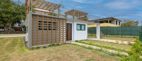 Une maison moderne avec un petit garage attenant, une pergola en bois et une pelouse bien entretenue.